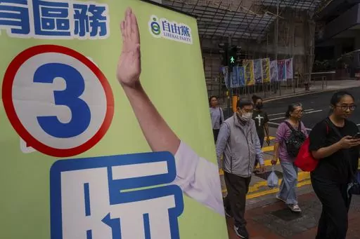 Pedestrians walk past a poster promoting a candidate during the District Council elections in Hong Kong, Sunday, Dec. 10, 2023. Residents went to the polls on Sunday in Hong Kong's first district council elections since an electoral overhaul was implemented under Beijing's guidance of “patriots” administering the city, effectively shutting out all pro-democracy candidates. (AP Photo/Louise Delmotte)