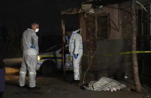 Police stand near a covered body in the Angelo settlement in Boksburg, South Africa, Thursday, July 6, 2023. Police said over a dozen people, including children, have died from a toxic gas leak in the informal settlement. (AP Photo/Themba Hadebe)