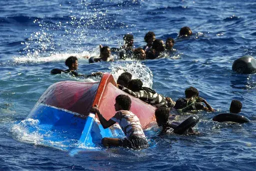 Migrants swim next to their overturned wooden boat during a rescue operation by Spanish NGO Open Arms at south of the Italian Lampedusa island at the Mediterranean sea, Aug. 11, 2022. Italy's new government has blocked humanitarian rescue ships from accessing its ports, resulting in a stand-off with charities that patrol the deadly central Mediterranean Sea smuggling routes, used by people desperate to reach Europe for a new life. (AP Photo/Francisco Seco, file)