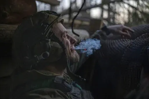A Ukrainian serviceman from the Azov brigade, known by the call sign Chaos, smokes a cigarette while he waits for a command to fire, in a dugout around one kilometer away from Russian forces on the frontline in Kreminna direction, Donetsk region, Ukraine, Friday, April 12, 2024. (AP Photo/Alex Babenko)