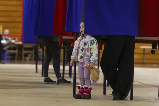 Elodie McCarran, 3, peaks out from a curtain as mother Lauren votes in Derry, N.H., Tuesday, March 11, 2025. (AP Photo/Reba Saldanha)