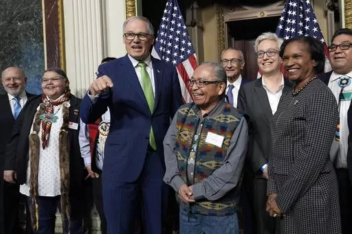 Washington Gov. Jay Inslee, third from left, stands with Chair Gerry Lewis of the Yakama Nation, fourth from left, as they and others pose for a photo following a ceremonial signing ceremony in Washington, Friday, Feb. 23, 2024. The ceremonial signing is an agreement between the Biden administration and state and Tribal governments to work together to protect salmon and other native fish, honor obligations to Tribal nations, and recognize the important services the Columbia River System provides