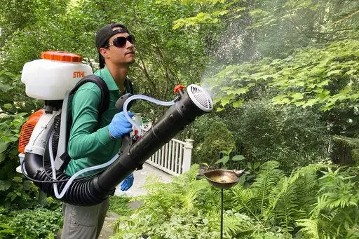 Mosquito Joe lead technician Damien Ysasi sprays a mixture of essential oil insecticides in a yard in Cascade Township near Grand Rapids, Mich., on July 20, 2022.  As climate change widens the insect's range and lengthens its prime season, more Americans are resorting to the booming industry of professional extermination. But the chemical bombardment worries scientists who fear over-use of pesticides is harming pollinators and worsening a growing threat to birds that eat insects. (AP Photo/John 