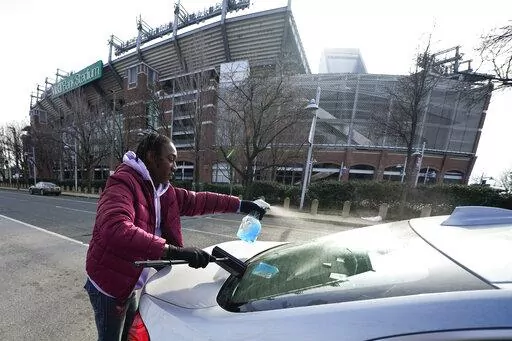 Shamonte Jones cleans the back windshield of a vehicle stopped at a red light near M&T Bank Stadium, Tuesday, Jan. 10, 2023, in Baltimore. Local officials are rolling out their latest plan to steer squeegee workers away from busy downtown intersections and toward formal employment using law enforcement action and outreach efforts. (AP Photo/Julio Cortez)
