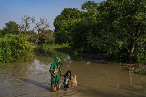A woman holds the hand of a child and wades through floodwaters along the banks of the river Yamuna in New Delhi, India, Wednesday, Sept. 28, 2022. For those living along the floodplains of the Yamuna River, being dislocated by floods has become a way of life. The latest displacement was an indirect consequence of extreme rainfall in upstream states in the Himalayan mountain region that resulted in the swelling of rivers and opening of many dams that were unable to accommodate the excess water. 