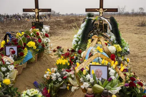 Flowers are placed around the graves of Ukrainian military servicemen Roman Rak and Mykola Mykytiuk in Starychi, western Ukraine, Wednesday, March 16, 2022. Rak and Mykytiu were killed during Sunday's Russian missile strike on a military training base in Yavoriv. (AP Photo/Bernat Armangue)