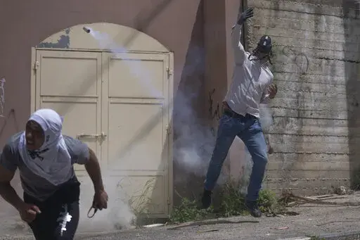 A Palestinian protester returns a teargas canister during clashes with Israeli border police in the West Bank village of Burqa, north of Nablus, Tuesday, April 19, 2022. Palestinians protesting against a settlers march toward Homesh, a settlement that was officially dismantled by Israel in 2005, clashed with Israeli border police that closed the main entrance of the village to secure the event. (AP Photo/Nasser Nasser)