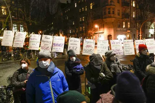 People wearing face masks stand next to posters calling for people to stick to coronavirus measures and not demonstrate with right-wing extremists and conspiracy theorists, at a counter-rally against anti-vaccination activists at the Gethsemane Church in Berlin, Germany, Monday, Jan. 24, 2022. A growing number of Germans have recently joined grassroots initiatives, local groups and spontaneous demonstrations to speak out against vaccination opponents, conspiracy theorists and far-right extremist