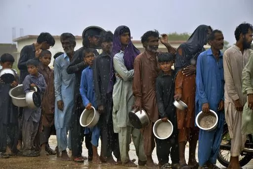 People wait in the rain for their turn to receive free food distributed by volunteers outside a camp of internally displaced people from coastal areas in Sujawal, Pakistan's southern district in the Sindh province, Thursday, June 15, 2023, as Cyclone Biparjoy was approaching. A vast swath of western India and neighboring southern Pakistan that suffered deadly floods last year are bracing for a new deluge as fast-approaching Cyclone Biparjoy whirls toward landfall Thursday. (AP Photo/Pervez Masih