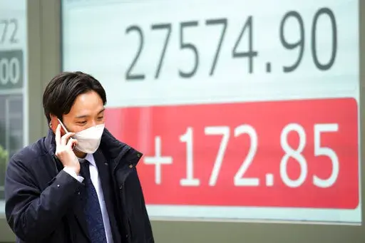 A person wearing a protective mask walks in front of an electronic stock board showing Japan's Nikkei 225 index at a securities firm Friday, Feb. 3, 2023, in Tokyo. Asian shares were trading mixed Friday ahead of a closely watched U.S. jobs report that may affect global interest rates. (AP Photo/Eugene Hoshiko)