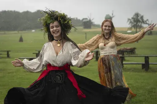 Ukrainian young women dressed in traditional clothing dance under heavy rain at a traditional Midsummer Night celebration near capital Kyiv, Ukraine, Sunday, June 23, 2024. The age-old pagan festival is still celebrated in Ukraine amid the third year of Russia-Ukraine war. (AP Photo/Efrem Lukatsky)