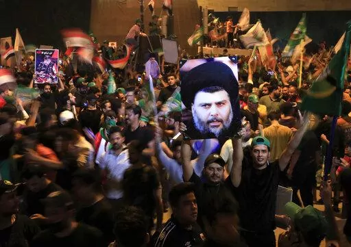 Followers of Shiite cleric Muqtada al-Sadr, on the poster, celebrate after the announcement of the results of the parliamentary elections in Tahrir Square, Baghdad, Iraq, Monday, Oct. 11, 2021. Eight months after national elections, Iraq still doesn't have a government. Driven by cutthroat competition for power and resources between elites, there is no clear way out of the unprecedented impasse. (AP Photo/Hadi Mizban, File)
