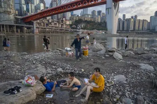People sit in a shallow pool of water in the riverbed of the Jialing River, a tributary of the Yangtze, in southwestern China's Chongqing Municipality, Saturday, Aug. 20, 2022. The very landscape of Chongqing, a megacity that also takes in surrounding farmland and steep and picturesque mountains, has been transformed by an unusually long and intense heat wave and an accompanying drought. (AP Photo/Mark Schiefelbein)