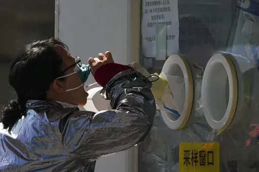 A woman pulls her face mask to get her routine COVID-19 throat swab at a coronavirus testing site in Beijing, Thursday, Oct. 6, 2022. Sprawling Xinjiang is the latest Chinese region to be hit with sweeping COVID-19 travel restrictions, as China further ratchets up control measures ahead of a key Communist Party congress later this month. (AP Photo/Andy Wong)