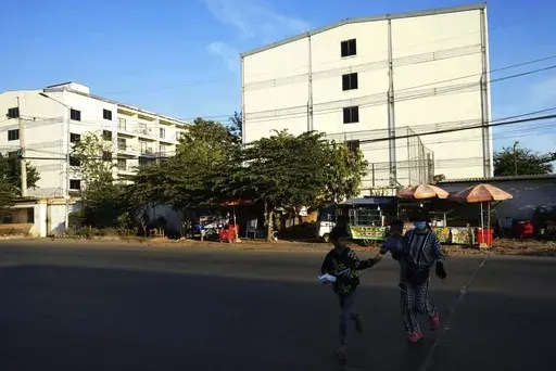 A family runs across the street near a building, where some people trafficked under false pretenses are forced to work in online scams targeting people all over the world, in Phnom Penh, Cambodia, Sunday, Feb. 9, 2025. (AP Photo/Heng Sinith)