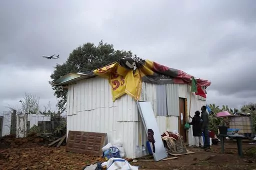 FILE Daisy and a friend attach a Portuguese flag to her makeshift house while a low-cost airline jet approaches for landing in Lisbon, in Loures, Portugal, Monday, March 6, 2023. Daisy was hoping the flag could provide some kind of protection, before the arrival of municipal workers sent to demolish the house. Seven families, mostly immigrants from Sao Tome & Principe, were evicted and had their illegal houses demolished. They had built their houses in the last couple of years when unable to pay