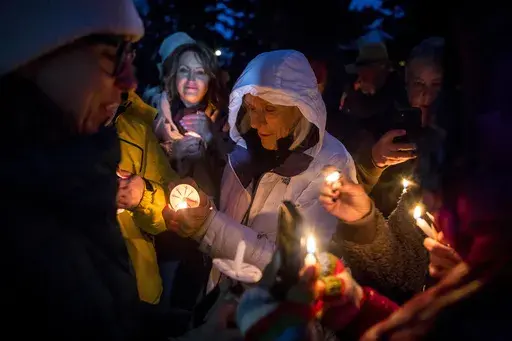 Rosalis Estes, center, keeps her candle lit in the drizzle at a vigil for grizzly bear No. 399 in Jackson, Wyo., Saturday Nov. 2, 2024. (AP Photo/Amber Baesler)