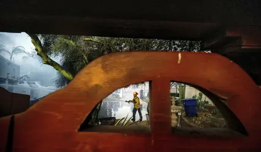 A firefighter hoses down the garage of Noel Piri's home that was destroyed by the Hawarden Fire in Riverside, Calif., on Sunday, July 21, 2024. (Terry Pierson/The Orange County Register via AP)