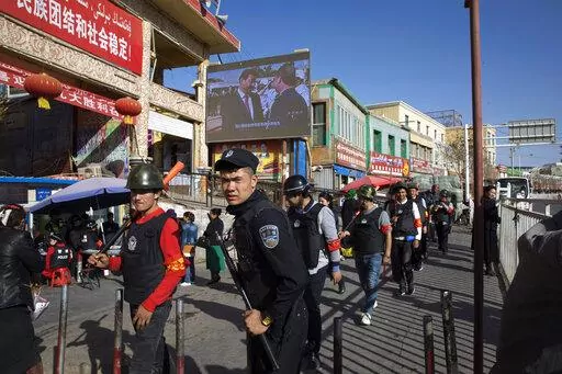 Armed civilians patrol the area outside the Hotan Bazaar where a screen shows Chinese President Xi Jinping in Hotan in western China's Xinjiang region, Nov. 3, 2017. China's discriminatory detention of Uyghurs and other mostly Muslim ethnic groups in the western region of Xinjiang may constitute crimes against humanity, the U.N. human rights office said in a long-awaited report Wednesday, Aug. 31, 2022, which cited "serious" rights violations and patterns of torture in recent years. (AP Photo/Ng