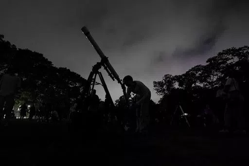 A girl looks at the moon through a telescope in Caracas, Venezuela, on Sunday, May 15, 2022. Six planets will line up in the early morning sky on June 3, 2024 but most won't be visible to the naked eye. A planetary parade happens relatively often when several planets align on the right side of the sun, making them visible across a narrow band of our sky. (AP Photo/Matias Delacroix)