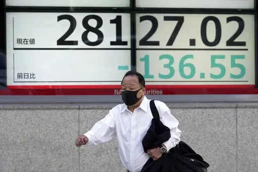 A person wearing a protective mask walks in front of an electronic stock board showing Japan's Nikkei 225 index at a securities firm Monday, Nov. 14, 2022, in Tokyo. Asian shares were mixed in Monday trading, as some momentum of a rally on Wall Street last week lost steam, amid varied sentiments about coronavirus restrictions easing in China and global interest rate hikes.  (AP Photo/Eugene Hoshiko)