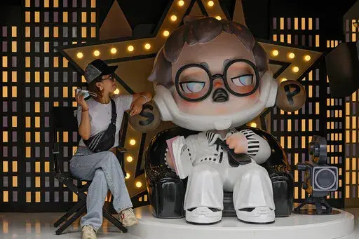 A woman holding her face mask poses with a toy figure on display at a popular shopping street in Shanghai, China, Sunday, Aug. 29, 2021. (AP Photo/Andy Wong)