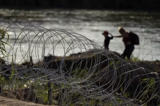 Migrants walk along concertina wire as they try to cross the Rio Grande at the Texas-U.S. border in Eagle Pass, Texas, Thursday, July 6, 2023. (AP Photo/Eric Gay)