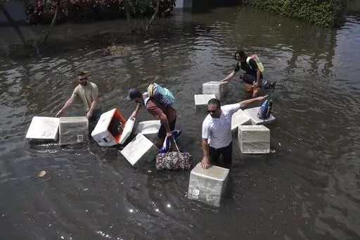 People try and save valuables as they wade through flood waters in the Edgewood neighborhood of Fort Lauderdale, Fla., April 13, 2023. Over 25 inches of rain fell in South Florida since Monday, causing widespread flooding. (Joe Cavaretta/South Florida Sun-Sentinel via AP)