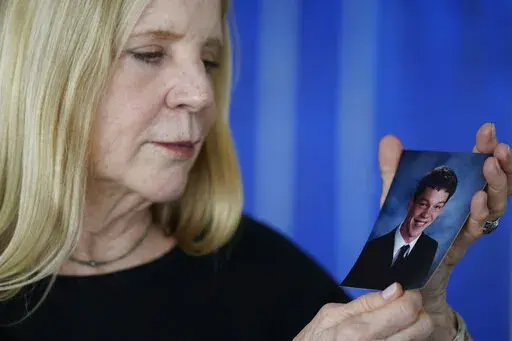 Dede Yoder poses for a picture with a photo of her son, Chris Yoder, after making a statement during a hearing in New York, Thursday, March 10, 2022. People who lost loved ones or years of their own lives to opioid addiction are getting their first and perhaps only chance to confront members of the Sackler family who own OxyContin maker Purdue Pharma. Thursday's virtual court hearing is being run by a U.S. Bankruptcy Court judge. (AP Photo/Seth Wenig)