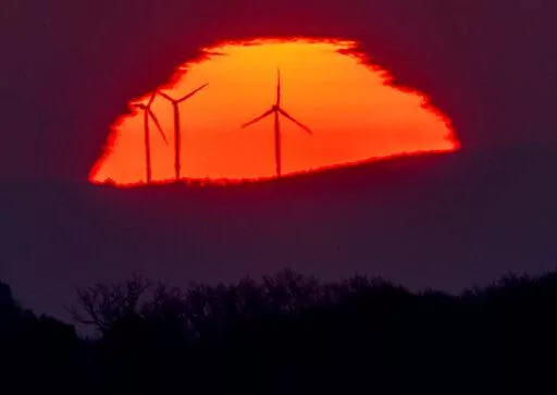 Wind turbines stand in front of the rising sun in Frankfurt, Germany, Friday, March 11, 2022. A United Nation-backed panel plans to release a highly anticipated scientific report on Monday, April 4, 2022, on international efforts to curb climate change before global temperatures reach dangerous levels. (AP Photo/Michael Probst, File)