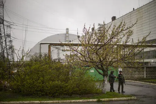 Ukrainian soldiers stand guard in front of the 'sarcophagus' steel structure, top left, that shelters the reactor 4 at the Chernobyl nuclear power plant, in Chernobyl, Ukraine, Tuesday, April 26, 2022. (AP Photo/Francisco Seco)