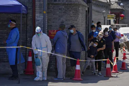 A worker in protective suit sprays disinfectant as residents line up for mass COVID test on Monday, May 16, 2022, in Beijing. Authorities say most of Shanghai has stopped the spread of the coronavirus in the community and fewer than 1 million people remain under strict lockdown. China's largest city is moving toward reopening as economic data showed the gloomy impact of China's "zero-COVID" policy. (AP Photo/Andy Wong)