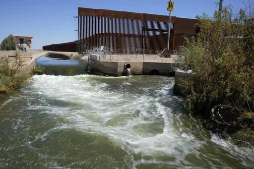 Water from the Colorado River flows in a canal along a border wall separating San Luis Rio Colorado, Mexico with San Luis, Arizona on Sunday, Aug. 14, 2022, in San Luis Rio Colorado, Mexico. By the time the Colorado River reaches Mexico, just a fraction of its water is left for the fields of the Mexicali Valley and millions of people in northwestern desert cities. (AP Photo/Gregory Bull)