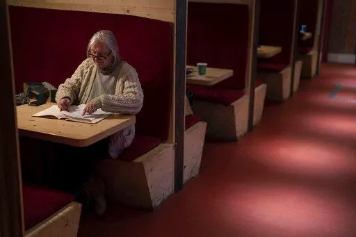 Wendy Freeman, an artist, writes poem at the Other Place theater, in Stratford-upon-Avon, Warwickshire, England, Tuesday, Feb. 28, 2023. The foyer of the Other Place theater in Shakespeare's birthplace of Stratford-upon-Avon is a cozy refuge from winter. One day a week the theater becomes a "warm hub," set up by the Royal Shakespeare Company to welcome people who may be struggling to heat their homes because of sky-high energy prices. (AP Photo/Kin Cheung)