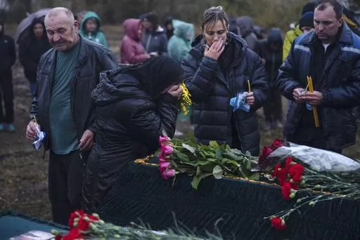 Relatives and friends mourn near the coffins of Tetiana Androsovych, 60, and Mykola Androsovych, 63, killed by a rocket strike, at a graveyard in the village of Hroza, near Kharkiv, Ukraine, Saturday, Oct. 7, 2023. The Ukrainian village of Hroza has been plunged into mourning by a Russian rocket strike on a village store and cafe that killed more than 50 people on Thursday, Oct. 5. (AP Photo/Alex Babenko)