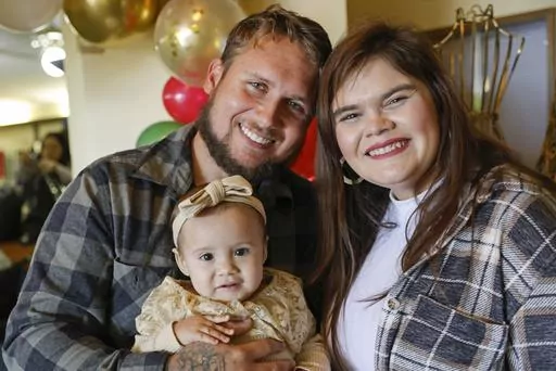 Alan Shurtleff, left, Morgan Shurtleff, right, and their daughter, 1-year-old Cora Dibert, pose for a photo at The Bridge Church, Saturday, Dec. 2, 2023, in Mustang, Okla. When Cora went for a routine blood test in October, the toddler brought along her favorite new snack: a squeeze pouch of WanaBana cinnamon-flavored apple puree. Within a week, the family got an alarming call. The test showed that the 1-year-old had lead poisoning, with nearly four times as much lead as the level that raises co