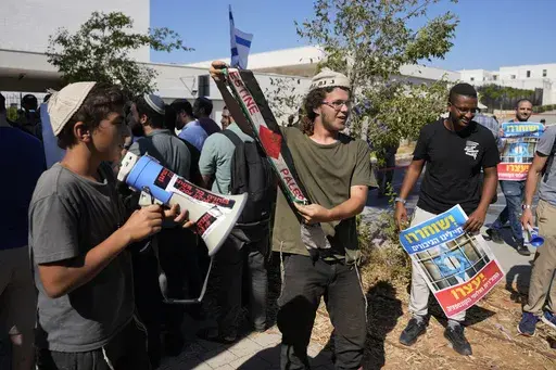 Right-wing Israelis, one holding a Palestinian scarf, at a protest outside of the initial hearing in military court for nine Israeli soldiers over what a defense lawyer said were allegations of sexual abuse of a Palestinian at a shadowy facility where Israel has held prisoners from Gaza during the war, in Beit Lid military base, Tuesday, July 30, 2024. (AP Photo/Ohad Zwigenberg)