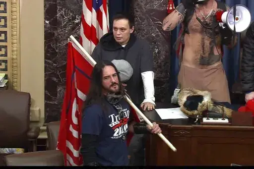 In this image from Senate Television video, Paul Allard Hodgkins, 38, of Tampa, Fla., front, stands in the well on the floor of the U.S. Senate on Jan. 6, 2021, at the Capitol in Washington. Hodgkins' attorney wrote in part, "This country has a long history of the public seeking to punish those who are perceived to have done wrong in 'their' eyes. .... A significant percentage of our population will 'cancel' Mr. Hodgkins because of 15-minutes of bad judgment, casting stones in his directions, al