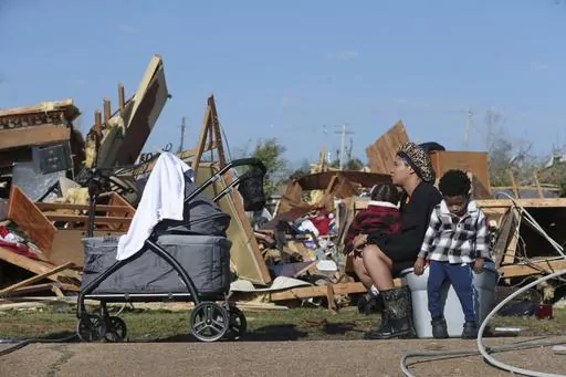 Melanie Childs of Amory, Miss., sits on a bucket and holds her two children, Mila, 1, left, and Major, 2, as they view whats left of her grandfather, Barrie Young, home Saturday 25, 2023. Emergency officials in Mississippi say several people have been killed by tornadoes that tore through the state on Friday night, destroying buildings and knocking out power as severe weather produced hail the size of golf balls moved through several southern states. (Thomas Wells/The Northeast Mississippi Daily