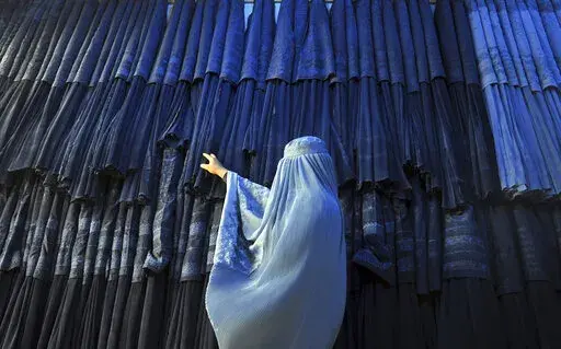 A woman clad in a burqa looks at other pieces of Afghanistan's traditional, all-encompassing dress at a store in Mazar-i Sharif, north of Kabul, Afghanistan, on Sept. 10, 2015. The Taliban announced they have arrested and will soon sentence an Afghan woman who appeared in a video on social media on Aug.  30, 2022, and said a senior Taliban official forced her into marriage and raped her repeatedly. (AP Photo/Mustafa Najafizada, File)