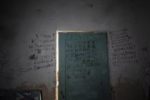 Writing can be seen on a wall and a door in the basement of a school in Yahidne, near Chernihiv, Ukraine, Tuesday, April 12, 2022. Residents say more than 300 people were trapped for weeks by Russian occupiers in  the basement of the school in Yahidne. They wrote the names of people who died during the Russian occupation of their village. (AP Photo/Evgeniy Maloletka)