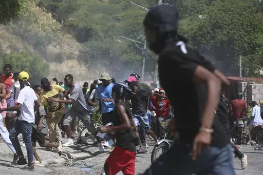 People run from tear gas fired by police to disperse protesters demanding police and the Prime Minister take immediate action against gangs in Port-au-Prince, Haiti, Monday, Aug. 19, 2024. (AP Photo/Odelyn Joseph)