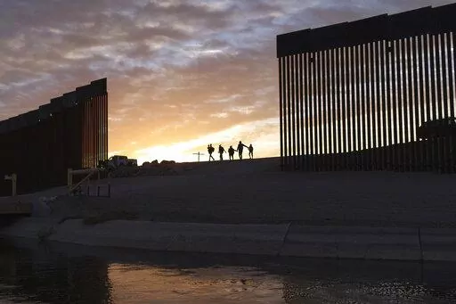 A pair of migrant families from Brazil passes through a gap in the border wall to reach the United States after crossing from Mexico in Yuma, Ariz., to seek asylum on June 10, 2021. The Biden administration may be ending asylum restrictions at the U.S.-Mexico border put in place to stop the spread of COVID-19, but the political and humanitarian challenges for the president may only get worse. (AP Photo/Eugene Garcia, File)