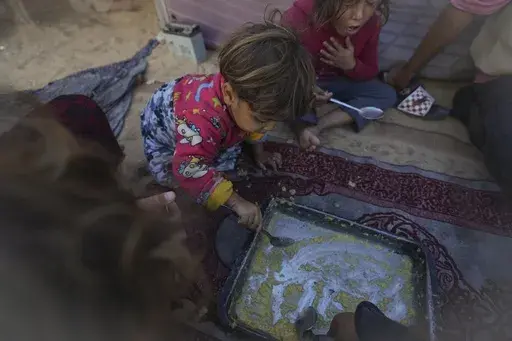 Girls in the Eid family eat lentils cooked by their mother, Yasmin, at their tent in a refugee camp in Deir al-Balah, Gaza Strip, Tuesday Nov. 19, 2024. (AP Photo/Abdel Kareem Hana)