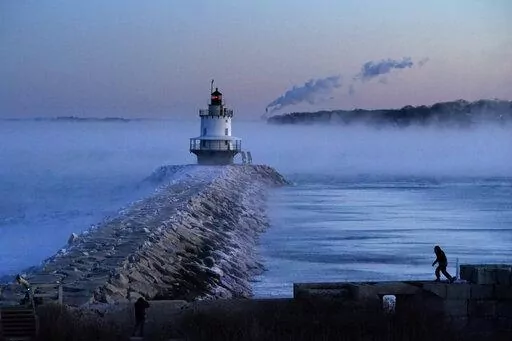 A man walks on sea wall near Spring Point Ledge Light, Saturday, Feb. 4, 2023, in South Portland, Maine. The morning temperature was about -10 degrees Fahrenheit. (AP Photo/Robert F. Bukaty)