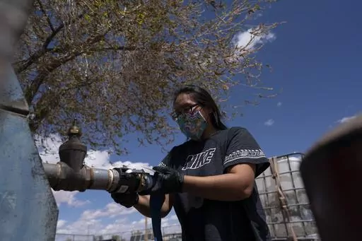 Raynelle Hoskie attaches a hose to a water pump to fill tanks in her truck outside a tribal office on the Navajo reservation, April 20, 2020, in Tuba City, Ariz. The Navajo Nation, a Native American tribe with one of the largest outstanding claims to water in the Colorado River basin, is closing in on a settlement with more than a dozen parties, putting it on a path to piping water to tens of thousands of tribal members in Arizona who still live without it. Negotiating terms outlined Wednesday, 