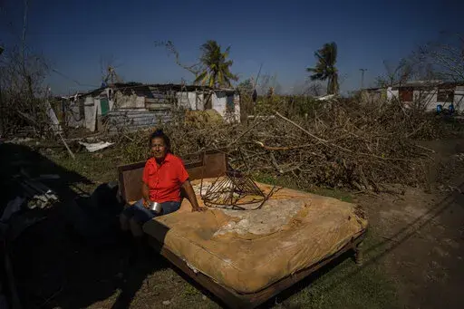 Mari Carmen Zambrano poses for a photo on her broken and wet bed as she dries it outside her home that lost its roof to Hurricane Ian in La Coloma, in the province of Pinar del Rio, Cuba, Wednesday, Oct. 5, 2022. (AP Photo/Ramon Espinosa, File)