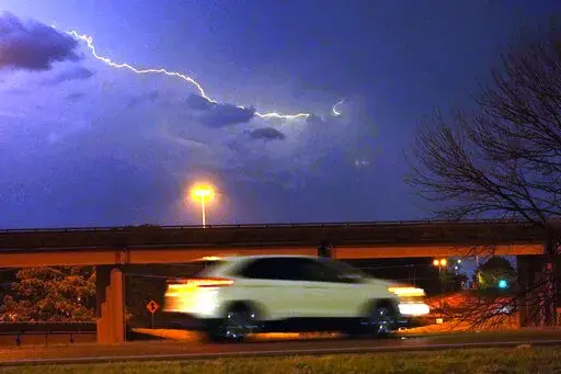 A vehicle races along a Jackson, Miss., street as lightning streaks across the sky, Tuesday evening, Nov. 29, 2022. Area residents were provided a light show as severe weather accompanied by some potential twisters affected parts of Louisiana and Mississippi. (AP Photo/Rogelio V. Solis)