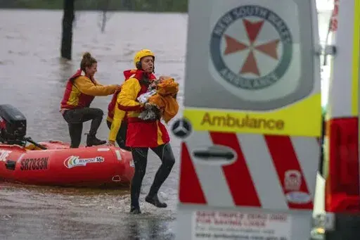 In this photo provided by the State Emergency Service, surf lifesaver Lee Archer carries a baby as the child and the mother are rescued from flood waters in Bulga, Australia, Wednesday, July, 6, 2022. Floodwaters were receding in Sydney and its surrounds on Thursday, July 7, 2022, as heavy rain continued to threaten to inundate towns north of Australia's largest city. (State Emergency Service via AP)