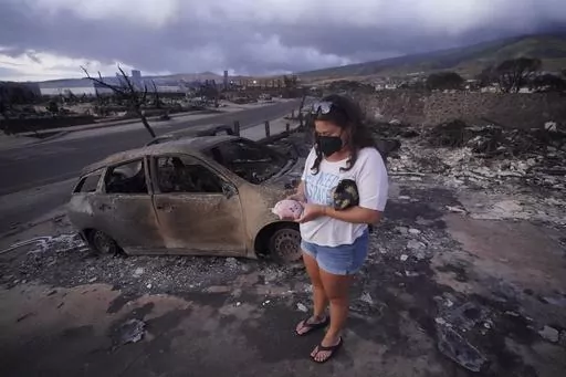 Summer Gerling picks up her piggy bank found in the rubble of her home following the wildfire on Aug. 10, 2023, in Lahaina, Hawaii. Lahaina residents are grappling with a range of feelings as Maui authorities plan to begin allowing them back into what has become known as the "burn zone." (AP Photo/Rick Bowmer, File)
